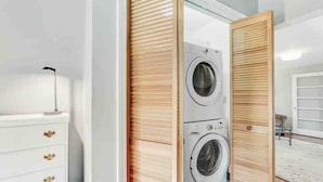 A modern laundry room with two stacked washing machines, a white dresser with gold handles, and a wooden sliding door.