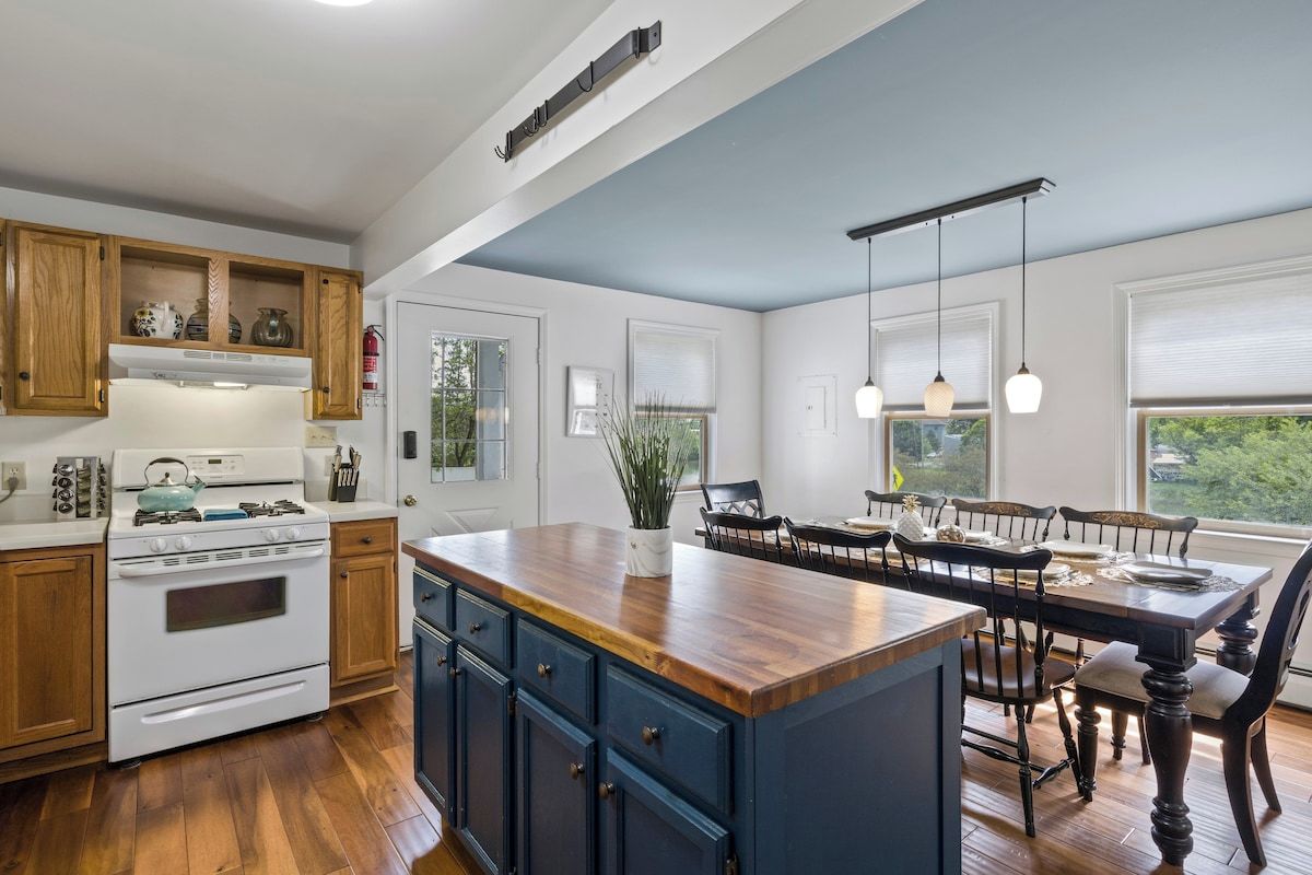 Una cocina con armarios de madera, una estufa blanca y un comedor con mesa y sillas de madera.