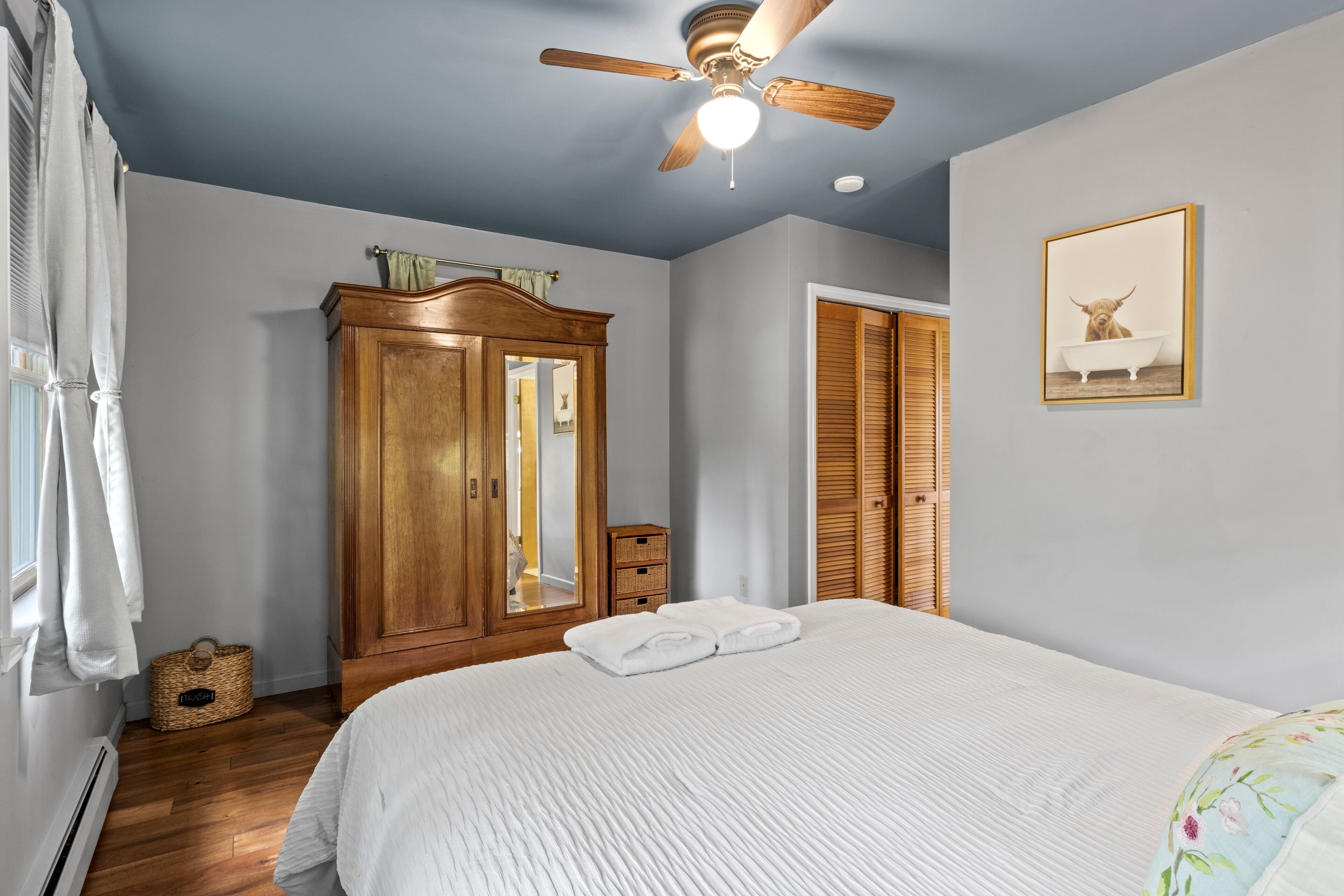 Ein Schlafzimmer mit einem Bett, einem Deckenventilator, einem Kleiderschrank, einem Spiegel und einem gerahmten Bild an der Wand.