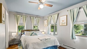 A bedroom with a bed, a ceiling fan, a window with curtains, a nightstand, and a rug.
