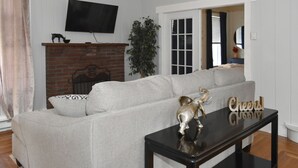 A living room with a sofa, a television mounted on the wall, a fireplace, and a small table with a decorative item. - Walk to Parks & Restaurants! (Watkins Glen)