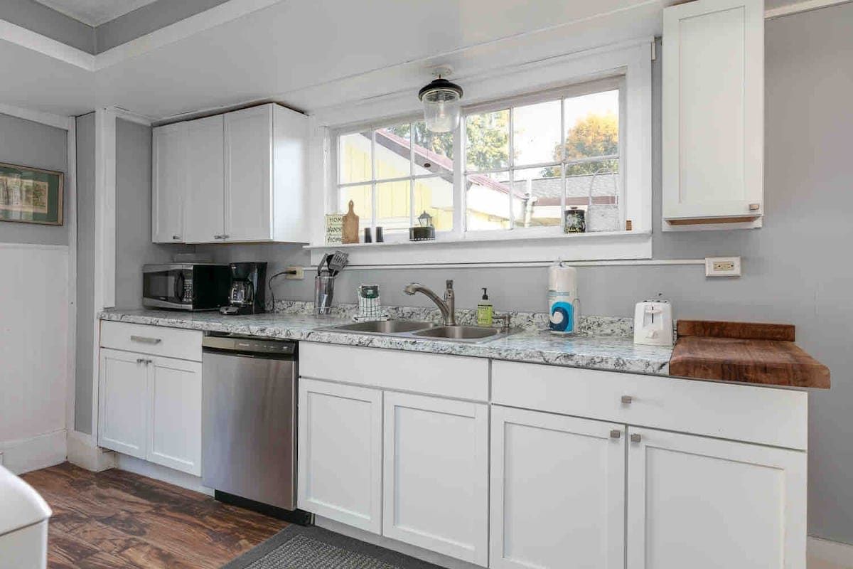 A kitchen with white cabinets, a microwave, a sink, and a window with a view of the outside.