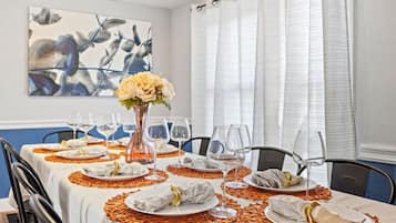 Uma sala de jantar com uma mesa posta para refeição, um vaso com flores e um quadro na parede.