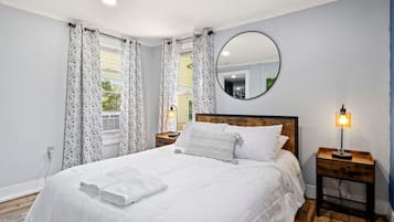 Quarto com cama grande, espelho redondo, abajur e janela com cortinas.