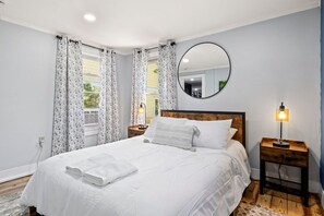 Une chambre à coucher avec un grand lit, un miroir rond, une lampe de chevet et une fenêtre avec des rideaux.