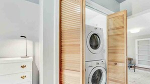 Une buanderie équipée de deux machines à laver superposées, d’une commode blanche aux poignées dorées et d’une porte coulissante en bois.