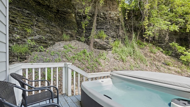 Un bain à remous sur une terrasse en bois, avec vue sur une falaise rocheuse et des arbres.