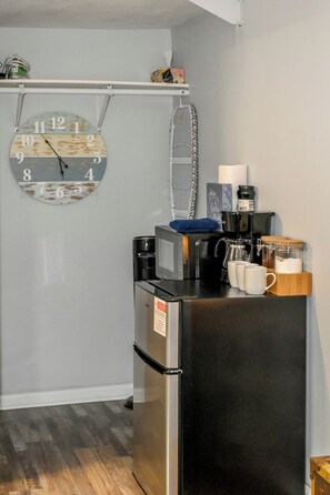 A compact kitchen with a refrigerator, microwave, and coffee maker. A clock is mounted on the wall above the counter. - Wine Trail Retreat | Walk to State Park | Downtown (Watkins Glen)