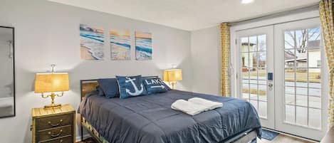 A bedroom with a bed, two bedside lamps, a nightstand, a rug, and artwork on the wall.
