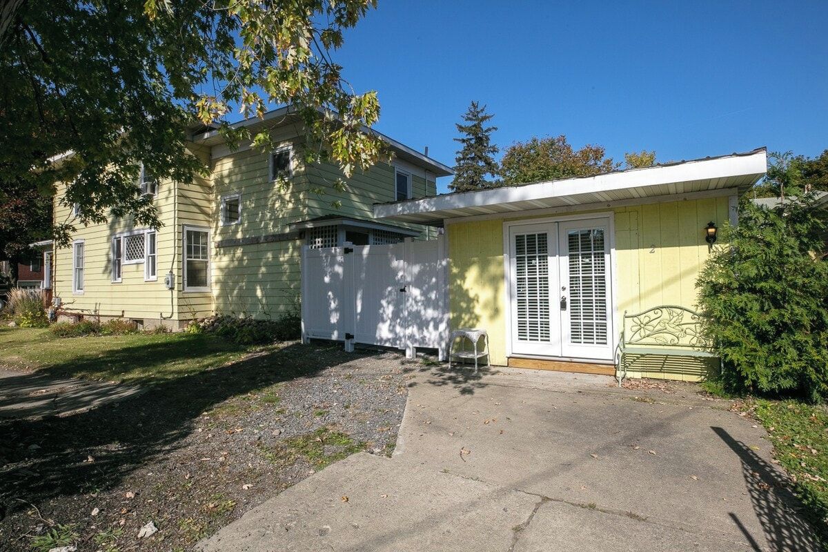 A two-story house with a front porch, a small attached garage, and a bench.
