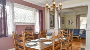A dining room with a wooden table set for six, surrounded by chairs, a chandelier, and a window with curtains.
