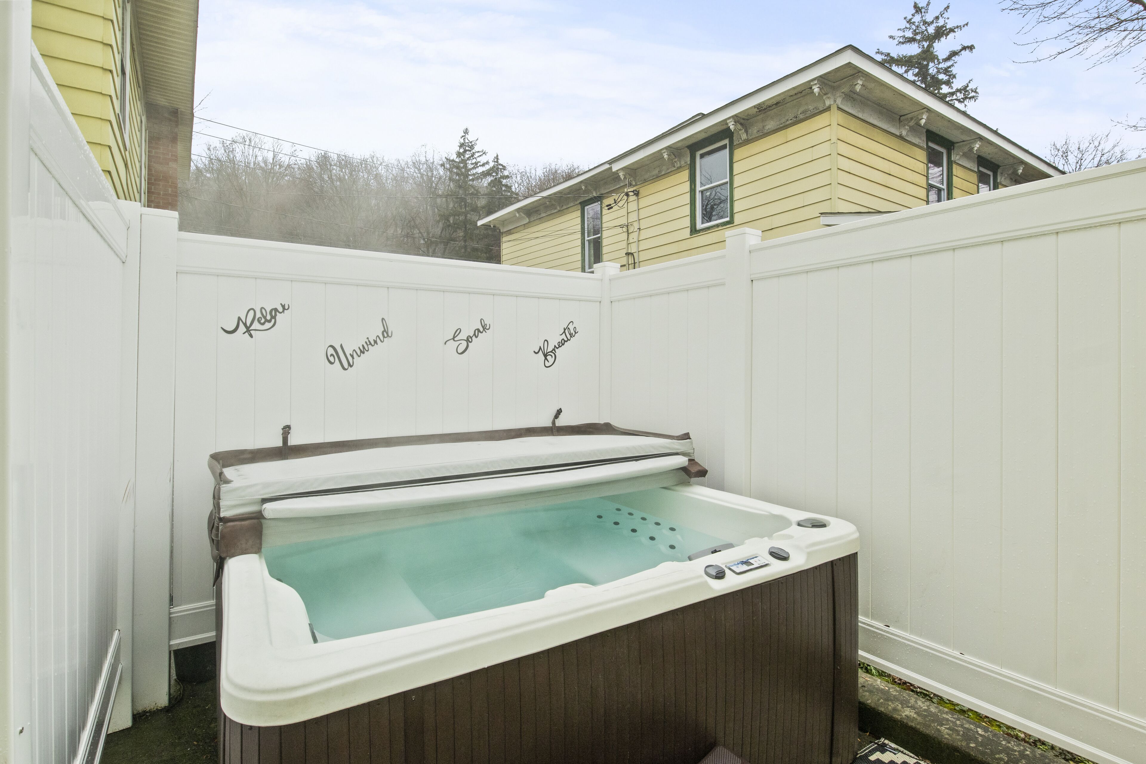 Een hottub met een houten buitenkant en een witte binnenkant, omringd door een witte omheining met tekst erop.