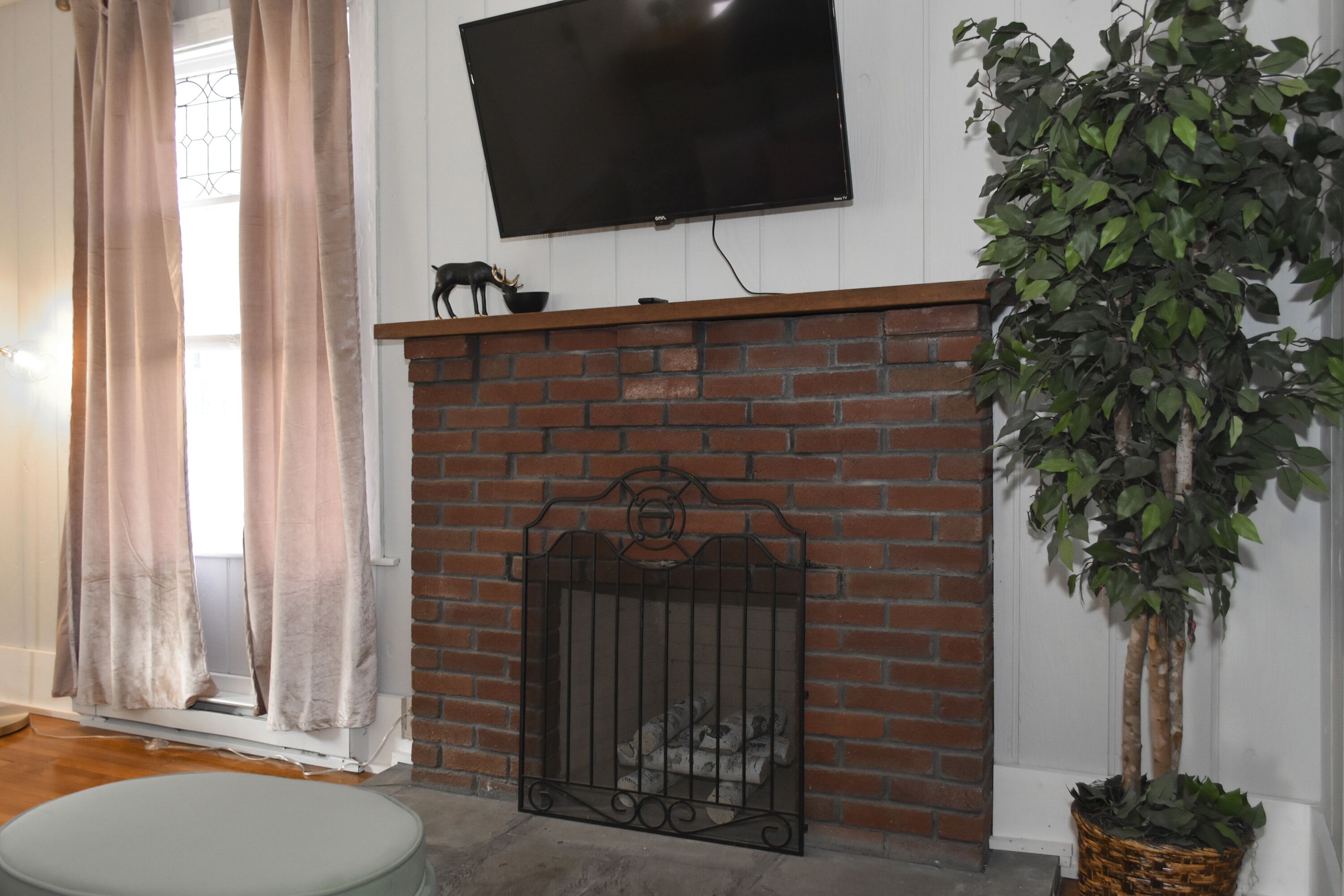 Una sala de estar con chimenea de ladrillo, un televisor montado encima y una planta en maceta a la derecha.