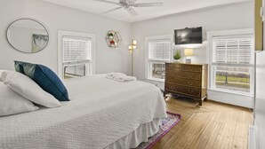 A bedroom with a bed, dresser, TV, and windows.