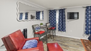 Une pièce avec un canapé en cuir rouge, une petite table accompagnée d’une chaise, un miroir décoratif et des rideaux à motifs bleus.