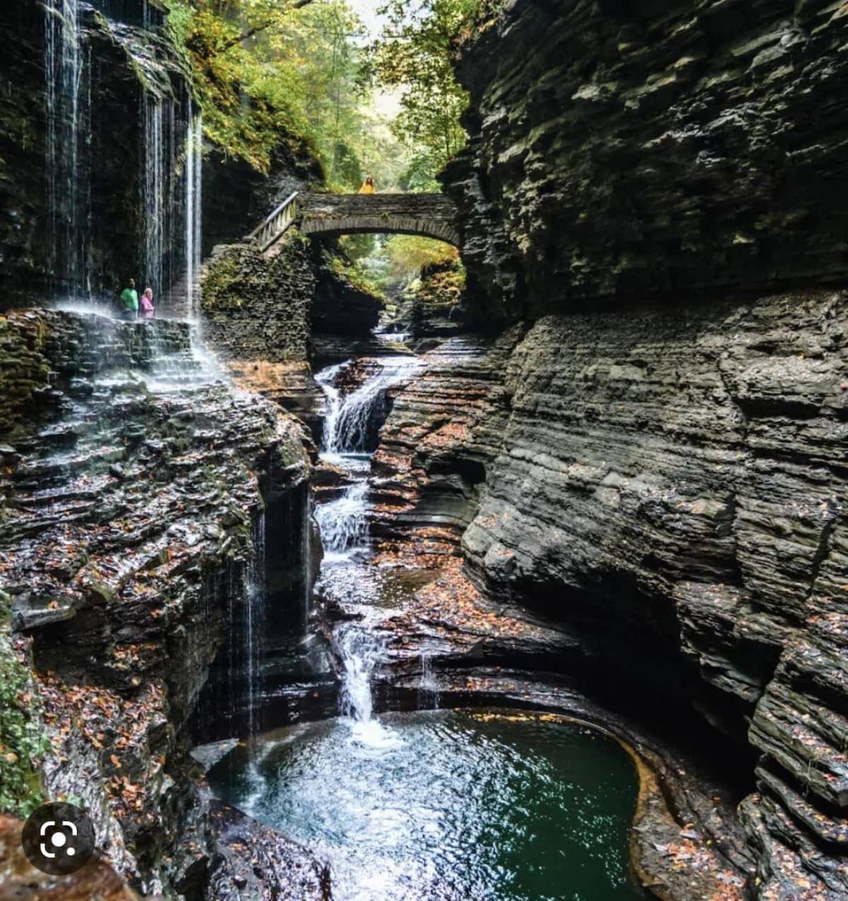A waterfall cascading over rocky terrain with a stone bridge in the background.