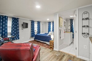 Una camera da letto con un letto, una sedia rossa, un tavolino, una TV e un bagno con uno specchio e un porta asciugamani.