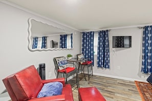 Une pièce avec un canapé en cuir rouge, une petite table avec des chaises, un miroir et des rideaux à motifs bleus.