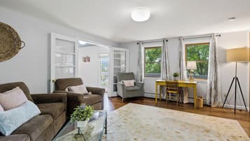 Ein Wohnzimmer mit einer Couch, Sesseln, einem Couchtisch und einem Schreibtisch mit einer Lampe.