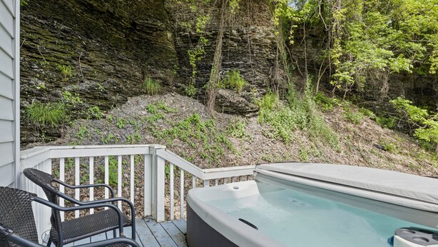 A hot tub on a wooden deck with a view of a rocky cliff and trees. - River Front! in the heart of Ithaca! (Ithaca)