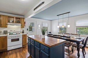Une cuisine avec des meubles en bois, un poêle blanc et un coin repas comprenant une table et des chaises en bois.