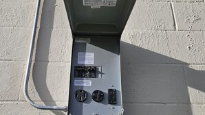 Een elektriciteitskast met een label, twee schakelaars en een aangesloten kabel.