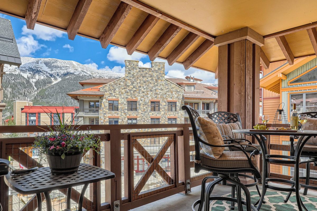 A balcony with outdoor furniture, a potted plant, and a view of snow-capped mountains.