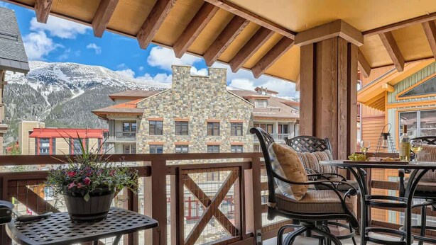 A balcony with a view of snow-capped mountains, a stone building, and a wooden pergola. - Luxury Slope & Village Views, Deck, Steps to Lifts (Frisco)