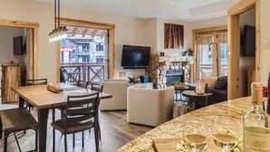 A cozy living area with a wooden dining table, comfortable seating, a fireplace, and a TV. - Luxury Slope & Village Views, Deck, Steps to Lifts (Frisco)