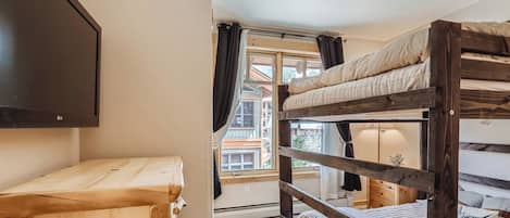 Habitación con literas, un televisor en la pared, un aparador de madera y una ventana con cortinas.