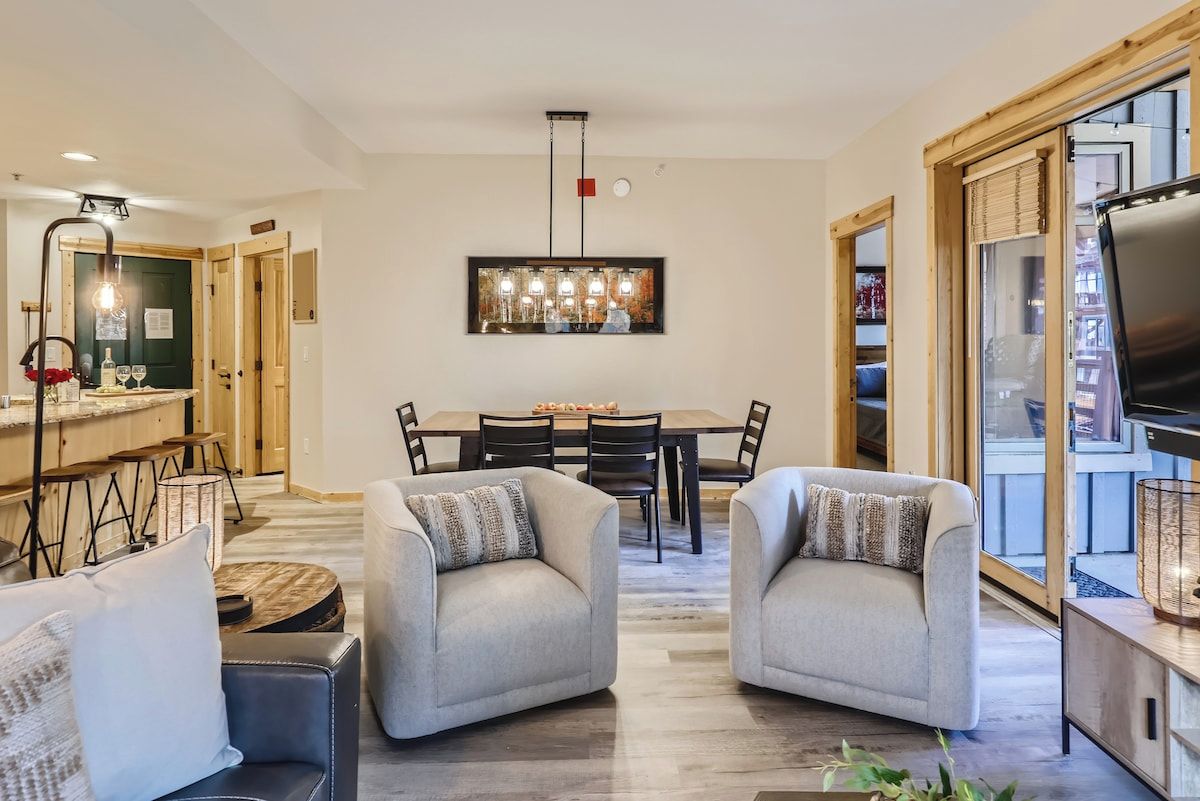 Un salon moderne avec deux fauteuils, une table à manger et un coin cuisine équipé de tabourets de bar.