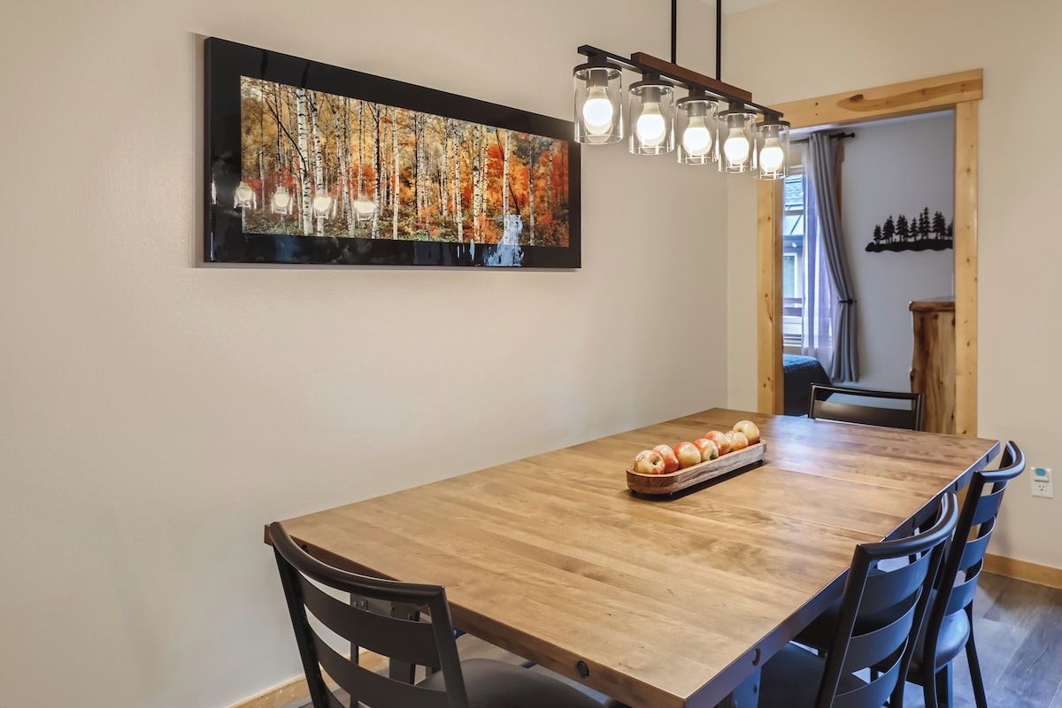 A dining area with a wooden table, chairs, a painting, and a light fixture.