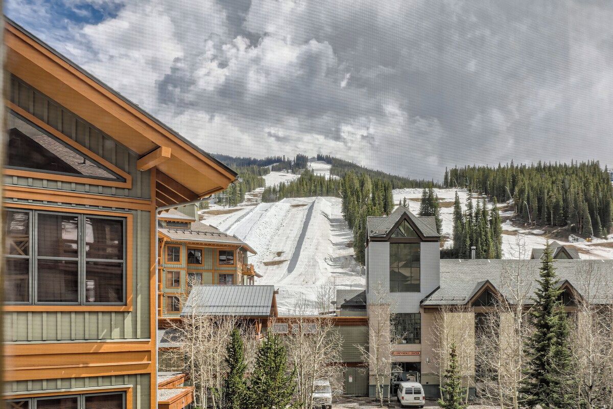 A hotel with a ski slope in the background, wooden architecture, and a clear sky.