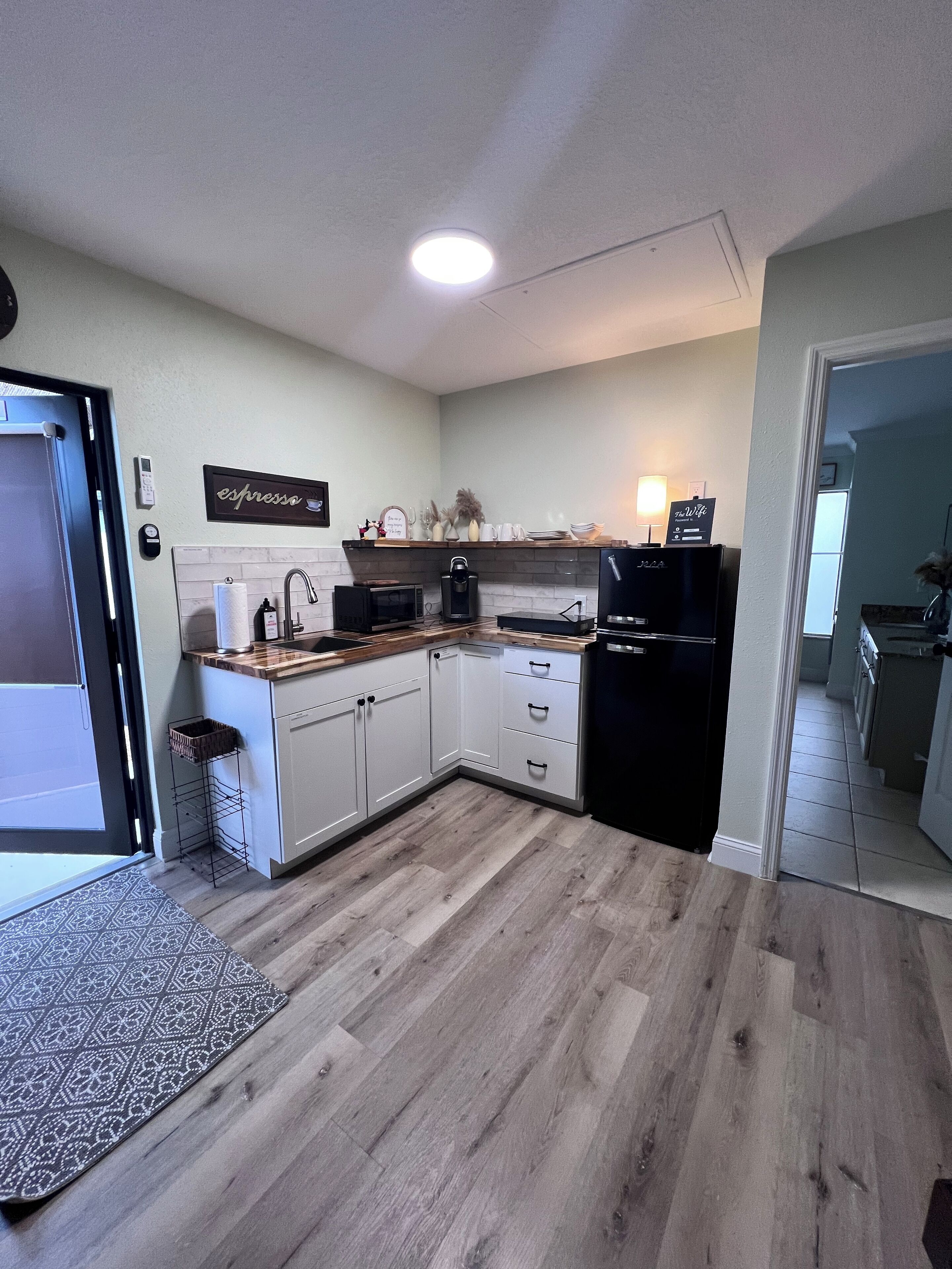 Une cuisine moderne avec des armoires blanches, un plan de travail en bois, un four à micro-ondes encastré et un réfrigérateur noir.