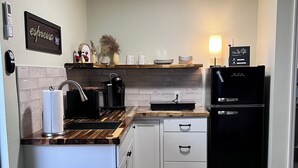 A modern kitchen with white cabinets, a black refrigerator, and a wooden countertop.