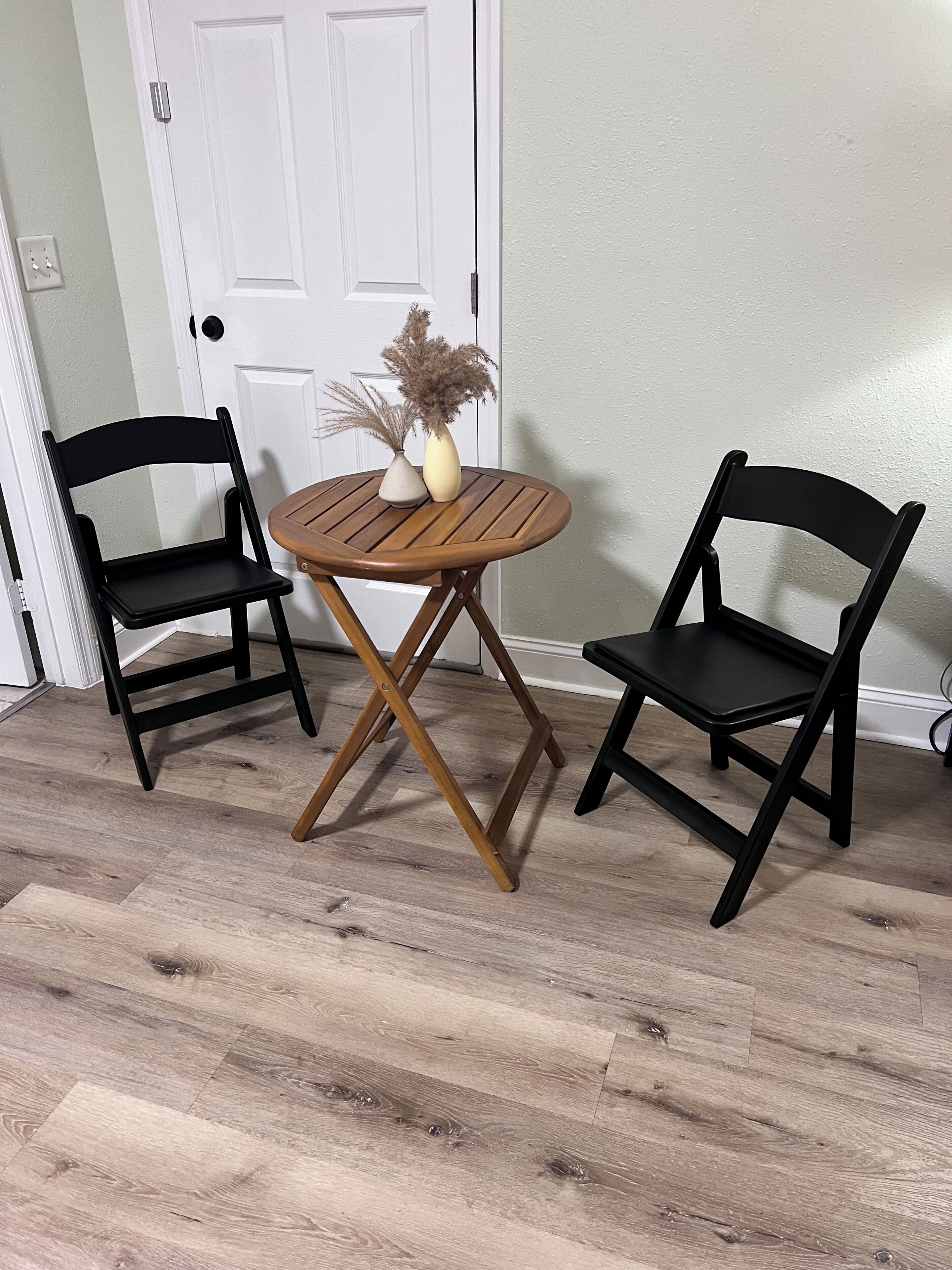 Une pièce avec deux chaises noires, une table ronde en bois et une porte blanche.