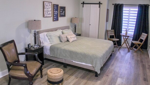 A bedroom with a bed, two nightstands, a chair, a small stool, and a window with curtains.
