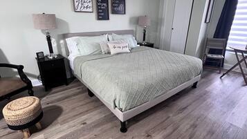 Une chambre bien rangée, avec un lit, des tables de chevet, une chaise et un petit tabouret.