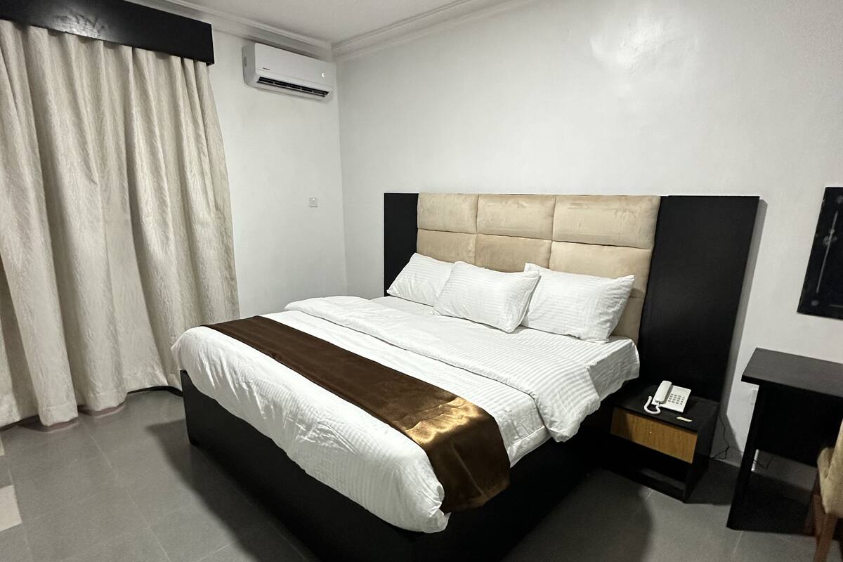 Une chambre d’hôtel moderne avec un grand lit, une table de chevet avec un téléphone et un petit bureau.