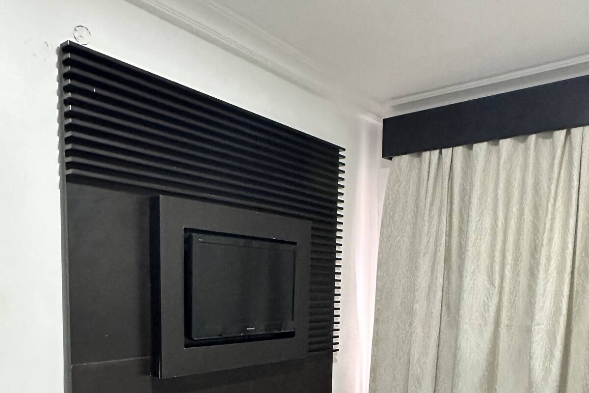 Une chambre d’hôtel avec un lit, un téléviseur fixé au mur et une fenêtre avec des stores.