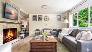 A living room with a fireplace, a sofa, a coffee table, and a large window with a view of greenery. - 1400sft Spacious SeaView Retreat & Garden surround (Federal Way)