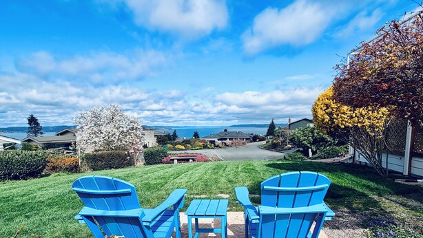 A patio with blue Adirondack chairs and a small table, a lawn, and a view of houses and a body of water. - 1400sft Spacious SeaView Retreat & Garden surround (Federal Way)
