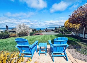 A patio with blue Adirondack chairs and a small table, a lawn, and a view of houses and a body of water. - 1400sft Spacious SeaView Retreat & Garden surround (Federal Way)