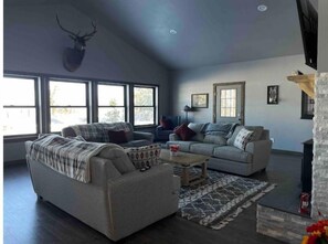 Relax in this spacious living room with a high ceiling, large windows, and a cozy fireplace.