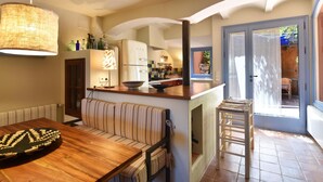Une cuisine chaleureuse avec un îlot central, un coin repas avec une table en bois et un canapé à rayures, et une vue sur l’extérieur grâce à une porte vitrée.