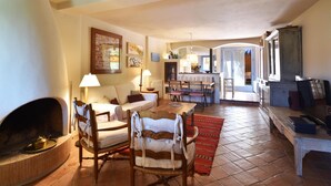 Un salon chaleureux avec une cheminée, un coin repas avec une table et des chaises, et une cuisine visible à travers une porte ouverte.