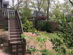 Stroll through the serene backyard, featuring a wooden staircase leading up to a deck surrounded by lush plants and a small garden.