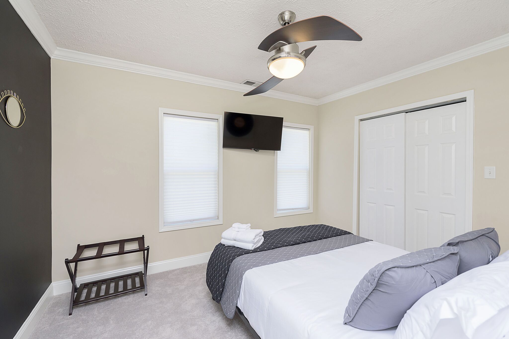 A bedroom with a bed, a bench, a ceiling fan, a TV, and a closet.