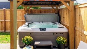 A hot tub with a wooden deck, two potted yellow flowers, and a bench.