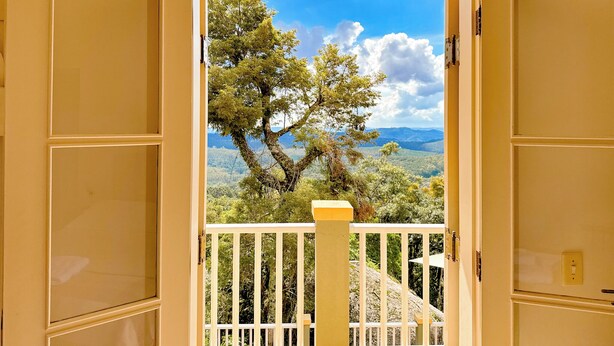 Une porte ouverte donnant sur un balcon d’où l’on peut admirer un arbre et des collines lointaines.